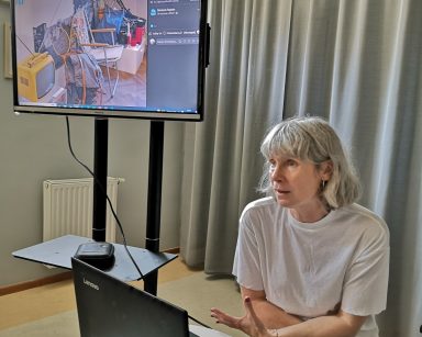 Sala. Edukatorka Iwona Zając z Muzeum Sopotu prowadzi siedzi przy laptopie. Prowadzi spotkanie.