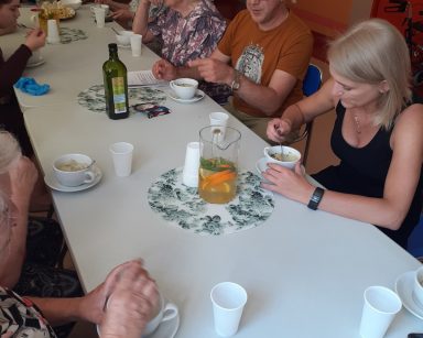 Seniorzy i pracownicy siedzą przy stole. Jedzą, rozmawiają.