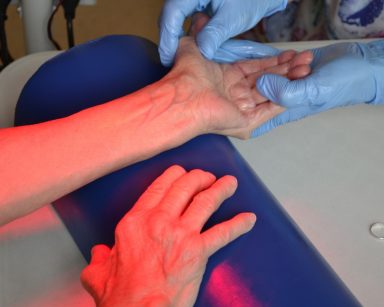Zabieg masażu. Zbliżenie. Fizjoterapeutka masuje dłonie seniorki pod lampą z czerwonym światłem.