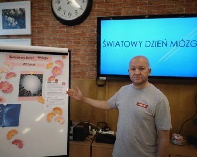 Sala. Kierownik Arkadiusz Wanat pokazuje tablicę flipchart. Za nim, na ekranie napis Światowy Dzień Mózgu.