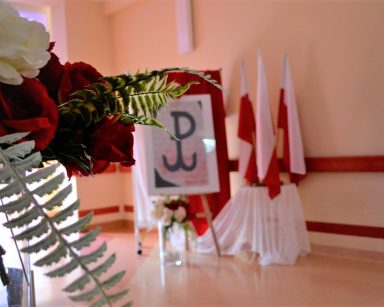 Korytarz. Dekoracja z okazji rocznicy Powstania Warszawskiego. Flagi, symbol polski walczącej, bukiet róż.