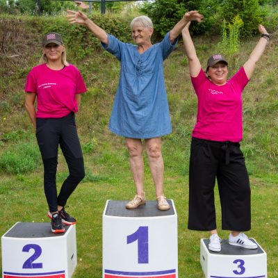 Plac na świeżym powietrzu. Na podium stoją seniorka, zastępczyni dyrektora Ilona Gajewska, terapeutka Gosia Jancelewicz.