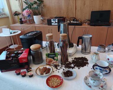 Na stole kawa, ekspres do kawy, filiżanki, mleko oraz przyprawy: anyż, kardamon, cynamon.