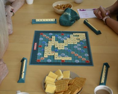 Cztery osoby grają w scrabble przy kawie i ciastkach.