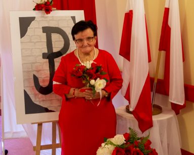 Pamiątkowe zdjęcie z obchodów Powstania Warszawskiego. Pozuje seniorka w czerwonej sukience.