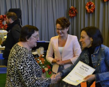 Sala. Na pierwszym planie seniorka. Wiceprezydentka Magdalena Czarzyńska-Jachim i dyrektorka Ewa Lewandowska dają jej dyplom.