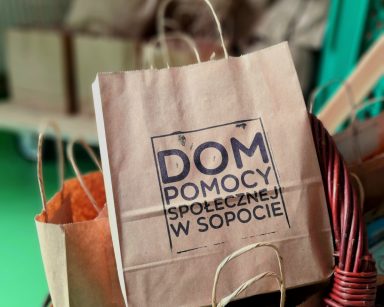 Zbliżenie na wiklinowy kosz. W koszu torebki prezentowe z napisem Dom Pomocy Społecznej w Sopocie.