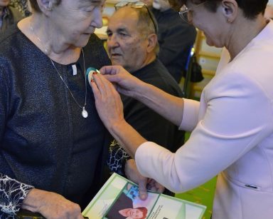 Sala. Na pierwszym planie wiceprezydentka Magdalena Czarzyńska-Jachim przypina medal seniorce.