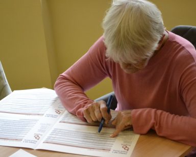 Sala. Seniorka wypełnia kartę do głosowania na Budżet Obywatelski.