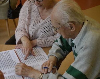 Sala. Seniorzy i pracownicy wypełniają karty do głosowania na Budżet Obywatelski.