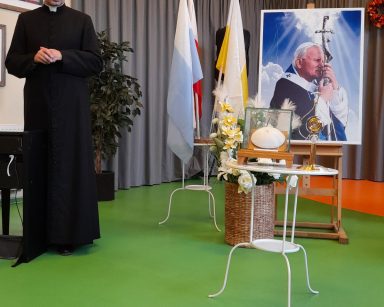 Sala. Ksiądz proboszcz Tomasz Kosewski stoi. Obok portret Jana Pawła II.
