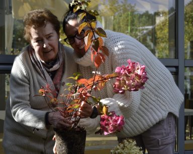 Pogodny dzień. Ogród. Terapeutka Magdalena Poraj-Górska i seniorka przesadzają kwiaty.