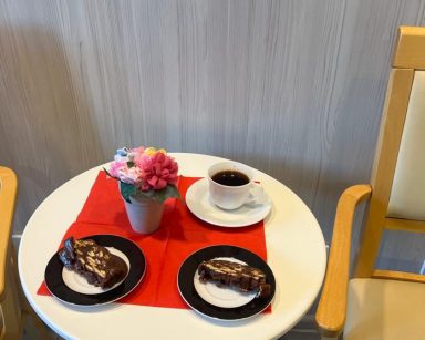 Widok z góry. Na stoliku dwa talerzyki z deserem, kubek z kawą, wazon z kwiatami.