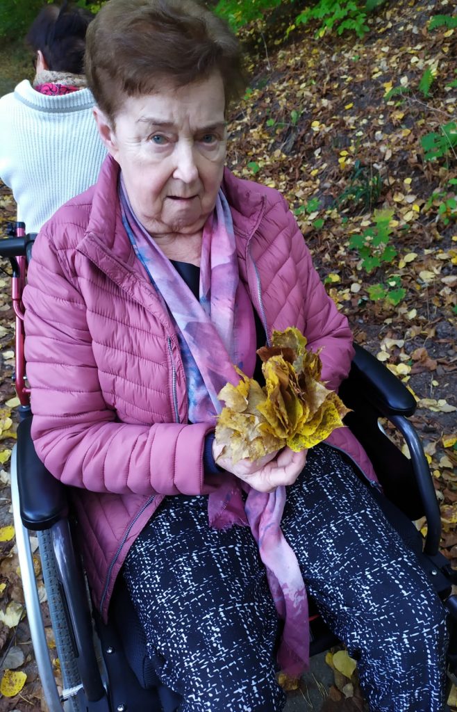 Las. Seniorka pozuje do zdjęcia. Trzyma bukiet z jesiennych liści.