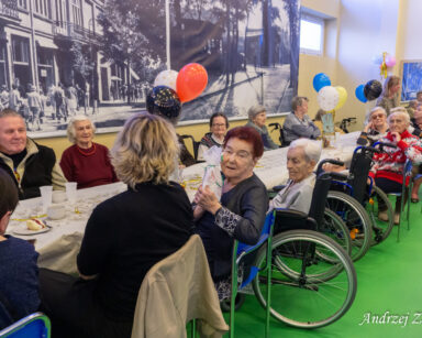Sala. Dekoracje z balonów. Przy stole siedzą pracownicy, seniorzy i wolontariusze.