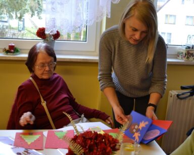 Sala. Na pierwszym planie zastępczyni dyrektora Ilona Gajewska i seniorka oglądają świąteczne kartki.
