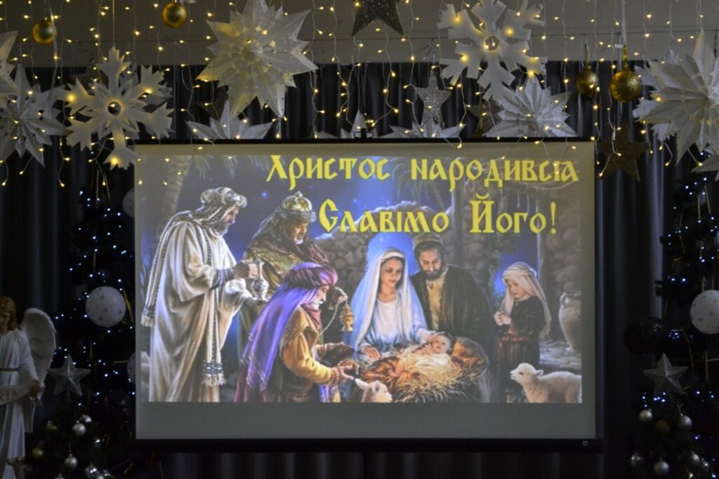 Sala udekorowana gwiazdami i lampkami. Na ekranie obraz z przybycia trzech króli do Jezusa i życzenia po ukraińsku.