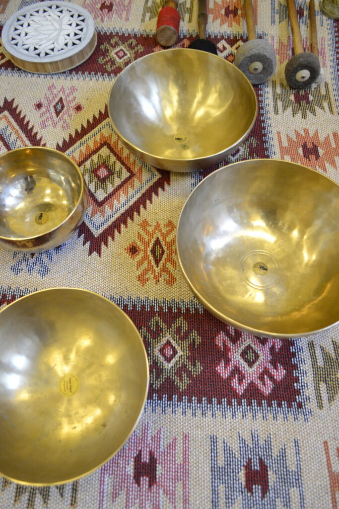 Widok z góry. Na dywanie rozłożone złote misy nepalskie do dźwiękoterapii.
