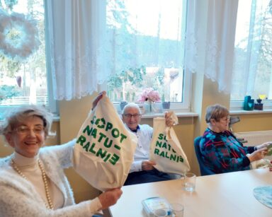 Sala. Na pierwszym planie senior i seniorka. Pokazują płócienne torby z napisem Sopot Naturalnie. Śmieją się.