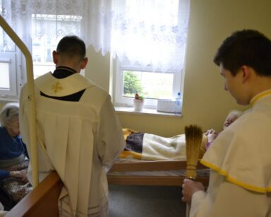 Pokój. Wizyta duszpasterska. Ksiądz Tomasz Kosewski i ministrant modlą się z dwoma seniorkami.