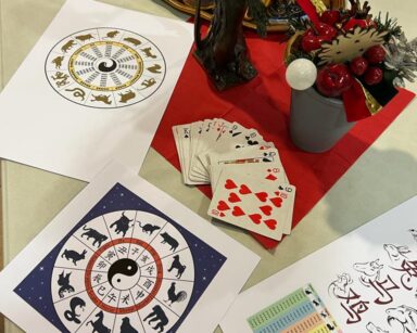 Widok z góry. Na blacie stołu taca z ciastkami, rozłożone kartki z symbolami z horoskopu chińskiego, karty do gry, ozdoby.