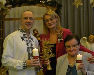Sala. Dyrektorka Agnieszka Cysewska, seniorka i Włodek Ivanets pozują do wspólnego zdjęcia. W tle szopka z Jezusem.