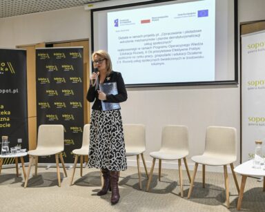 Sopoteka. Z mikrofonem stoi dyrektorka Agnieszka Cysewska. Za nią ekran z informacjami o debacie.