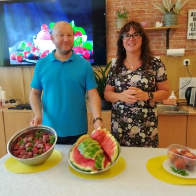 Sala. Kierownik Arkadiusz Wanat i dietetyczka Karolina Gorzkiewicz stoją przy stole z owocami.