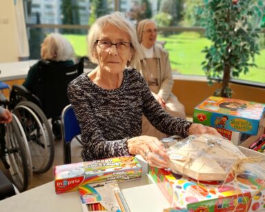 Ogród zimowy. Seniorzy przy stole z grami i materiałami plastycznymi.