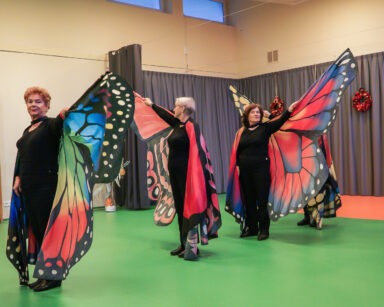 Sala. Cztery seniorki z grupy tanecznej ubrane w skrzydła motyla unoszą ręce.