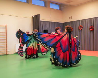 Sala. Cztery seniorki tańczą w parach. Na sobie mają kolorowe skrzydła motyla.