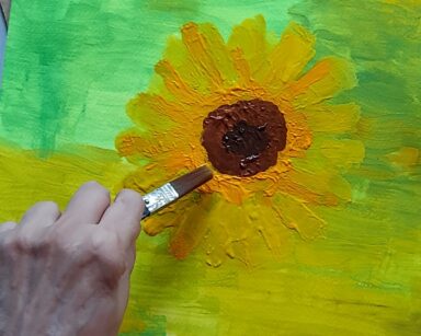 Zbliżenie. Obraz. Ręka kobiety maluje żółty kwiat na zielonym tle.