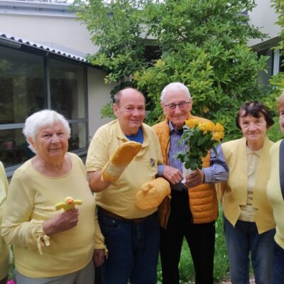 Zbliżenie. Grupa seniorów ubrana na żółto pozuje do zdjęcia. Jeden z mężczyzn trzyma w dłoni żółte róże.