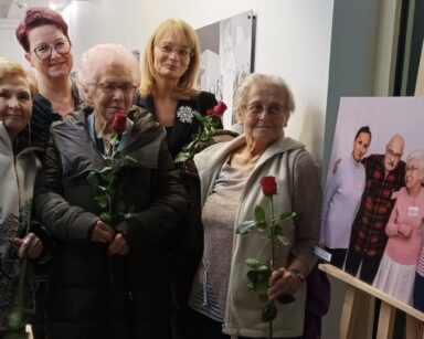 Zbliżenie. Pięć kobiet pozuje do zdjęcia. Kobiety trzymają w dłoniach róże. W tle na ścianach zdjęcia.