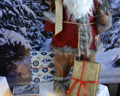Zbliżenie. Mikołaj stoi wśród prezentów. W tle pejzaż zimowy.