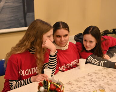 Zbliżenie. Trzy młode wolontariuszki siedzą przy stole. Na stole kubki i stroik.