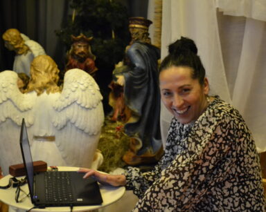 Zbliżenie. Uśmiechnięta kobieta siedzi przy laptopie. W tle figurki aniołów i trzech króli.