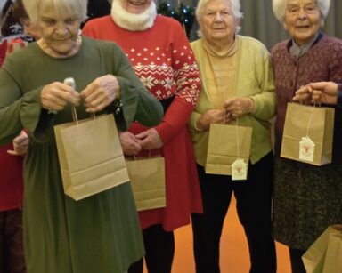 Zbliżenie. Cztery seniorki pozują do zdjęcia. W dłoniach trzymają świąteczne prezenty.