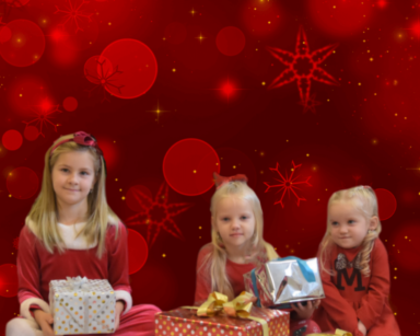 Zdjęcie. Czerwone tło ze złotymi gwiazdami. Trzy dziewczynki siedzą przy prezentach i się uśmiechają.