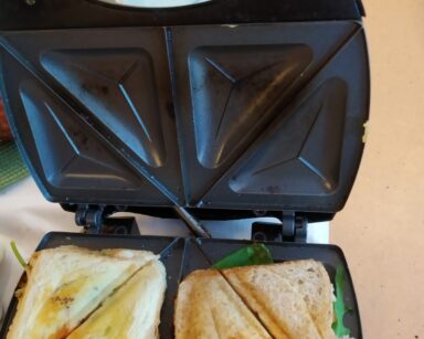 Zbliżenie. Toster. W tosterze kromki chleba przecięte na trójkąciki. Chleb ma rumianą skórkę i wystaje z niego sałata.