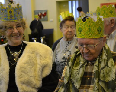 Sala. Czterech uśmiechniętych seniorów w koronach na głowie pozuje do zdjęcia.