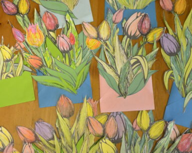 Zbliżenie. Blat. Na blacie wiele bukietów wyciętych i pomalowanych tulipanów, umieszczonych w kolorowych kopertach.