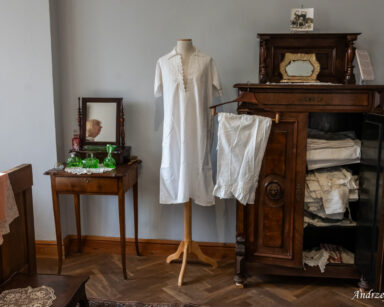 Pokój. Szafka z białą, koronkową, damską bielizną. Manekin w białej damskiej koszuli. Toaletka z lustrem i flakonami.