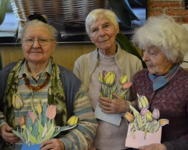 Zbliżenie. Trzy seniorki pozują do zdjęcia. W rękach trzymają wycięte i pokolorowane kwiaty.