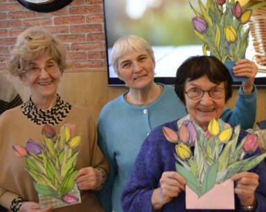 Zbliżenie. Uśmiechnięte seniorki pozują do zdjęcia z wyciętymi i pomalowanymi kwiatami.