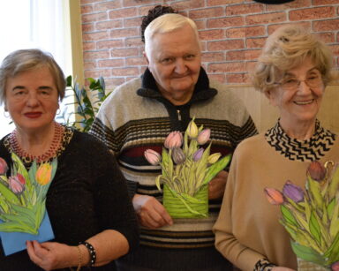 Zbliżenie. Troje seniorów z kwiatami w rękach pozuje do zdjęcia. Seniorzy uśmiechają się.