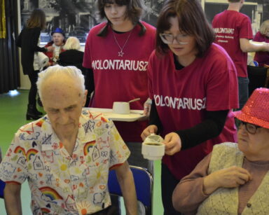 Zbliżenie. Dwie wolontariuszki podają filiżanki do stołu. Przy stole siedzą seniorzy.