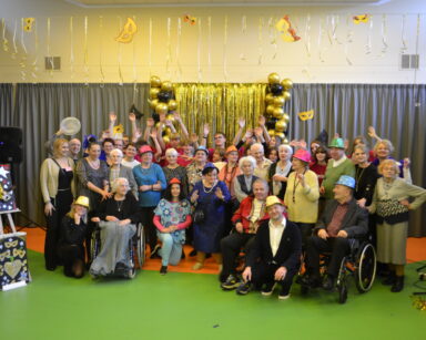 Sala. Scena. Grupa osób pozuje do wspólnego zdjęcia. W tle złota girlanda, maski, balony.