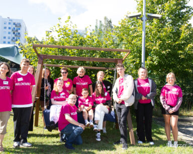 Grupa młodych wolontariuszy z seniorem wolontariuszem w różowych podkoszulkach pozują do zdjęcia grupowego.