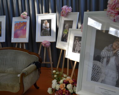 Sala. Kanapa, kwiaty, osiem zdjęci na sztalugach przedstawiające seniorki pozujące do zdjęcia. W tle zasłona.
